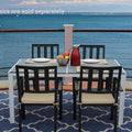 An outdoor dining scene featuring a rectangular composite wood dining table with a white frame, set against a stunning ocean view. The table is accompanied by black chairs with beige cushions, and there are place settings, a bowl of fruit, and a red pitcher on the table. Note: Chairs are sold separately. Rectangular Outdoor Dining Table with Ocean View (Chairs Sold Separately). rectangular outdoor dining table, composite wood table, white - framed table, outdoor chairs, ocean view dining