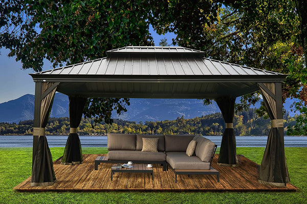 An outdoor hardtop gazebo with a sleek, metallic roof is set on a wooden deck in a picturesque natural setting. The gazebo features elegant, draped curtains and shelters a cozy lounge area with a sectional sofa, throw pillows, and a coffee table. The background showcases a serene lake, lush greenery, and distant mountains, creating a tranquil outdoor retreat. Tranquil Outdoor Gazebo: A Lakeside Retreat with Comfortable Seating. outdoor gazebo, lakeside gazebo, hardtop gazebo, comfortable seating.