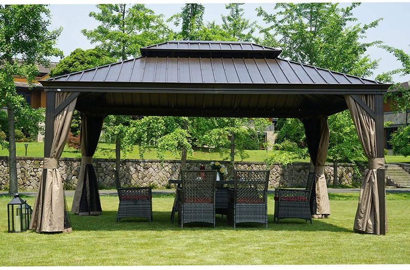 An outdoor hardtop gazebo with a dark - toned metal roof is set on a grassy lawn. The gazebo features earth - toned curtains that can be tied back, and underneath it, there is a wicker patio set with a table and chairs. Additionally, there are black lanterns placed on the grass nearby, enhancing the cozy outdoor ambiance.Cozy Outdoor Gazebo with Wicker Patio Set and Lanterns. outdoor gazebo, hardtop gazebo, wicker patio set, earth - toned curtains, black lanterns