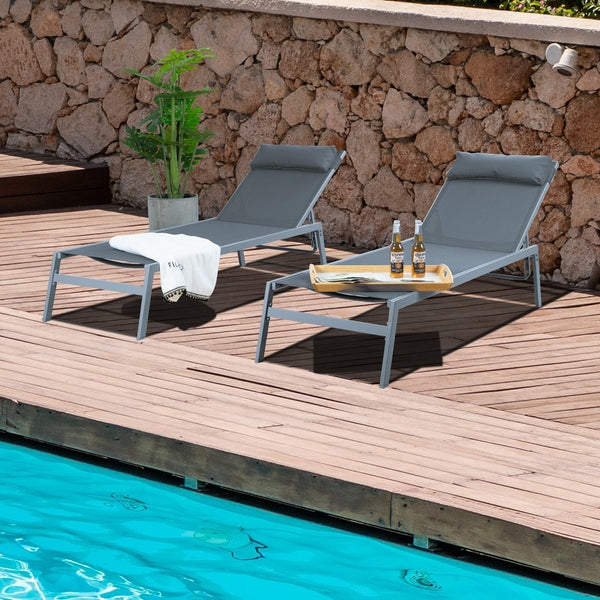 Title: Modern Poolside Lounge Chairs with Drinks and Towel
Alt Text: Two grey lounge chairs by a pool with a wooden deck, featuring a white towel, a tray with two beer bottles, and a stone wall backdrop.
Keywords: poolside lounge chairs, modern outdoor furniture, wooden deck, stone wall, relaxation, beer bottles, towel, summer vibe