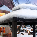 An outdoor gazebo covered in a thick layer of snow, with icicles hanging from the edge of its roof. The scene is set in a winter environment with a brick house in the background, partially illuminated windows suggesting warmth inside. Snow - laden bushes and trees add to the wintry atmosphere.Winter - Coated Outdoor Gazebo: A Snowy Retreat. outdoor gazebo, winter scene, snow - covered, icicles, brick house background.