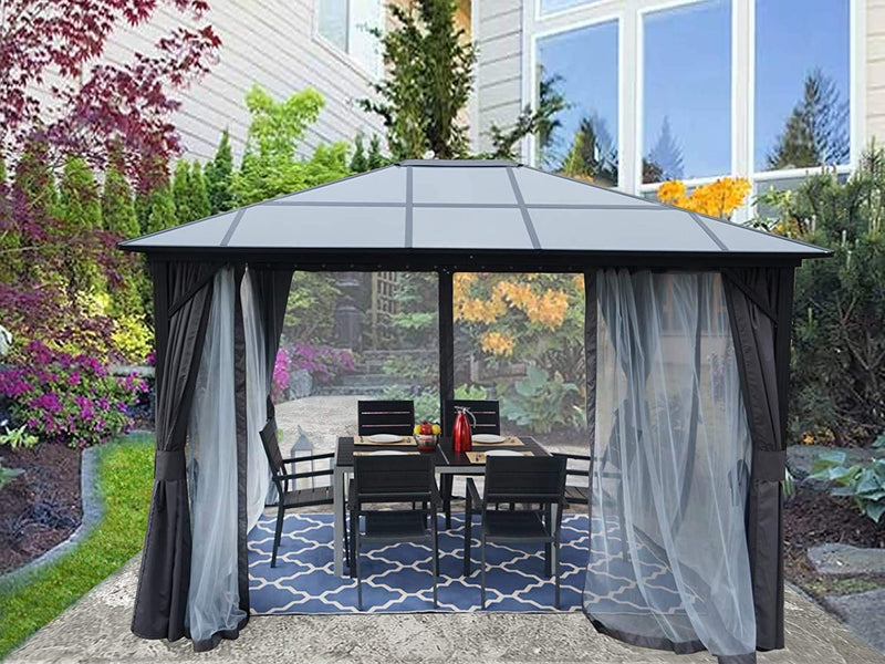 A stylish gazebo with a modern, dark - colored roof stands on a patio adjacent to a home. It is equipped with dark privacy curtains and sheer mesh panels, providing both seclusion and protection from bugs. The gazebo houses a black outdoor dining set, and the area is enhanced by the lush plants and colorful blooms in the background. Modern Outdoor Gazebo: Ideal for Garden Dining. Stylish Gazebo with Mesh and Curtains for Outdoor Relaxation. outdoor gazebo, garden gazebo, mesh netting, privacy curtains