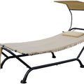An outdoor hammock - style lounger with a beige fabric bed, a small cushion, and a canopy. It has a black metal frame and a side pocket, and the bottom edge of the fabric features a fringe design.Beige Outdoor Hammock Lounger with Canopy. outdoor hammock lounger, beige hammock, canopy - equipped hammock, metal - framed hammock.