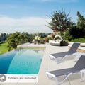Two modern outdoor lounge beds with sleek grey and white frames are placed beside a swimming pool in a luxurious outdoor setting. The lounge beds have adjustable backrests. A caption notes that "Table is not included." The background features lush greenery and a scenic view of a golf course. Modern Outdoor Lounge Beds by the Pool. outdoor lounge beds, swimming pool furniture, adjustable backrest, modern design, luxury outdoor setting. 