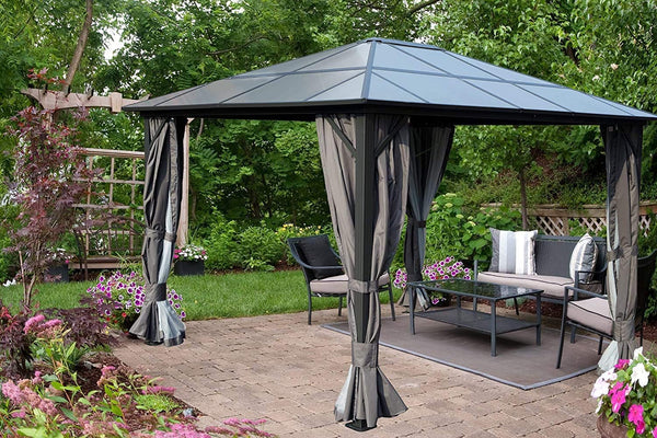A stylish outdoor gazebo with a dark - colored, geometric - patterned roof stands on a paved patio. The gazebo is adorned with elegant grey curtains that can be tied back, and it houses comfortable outdoor furniture including a sofa, chairs, and a coffee table. Surrounding the gazebo are lush green plants and vibrant flowers, creating a serene garden setting. Elegant Outdoor Gazebo: Perfect for Garden Relaxation. Stylish Gazebo in a Lush Garden Setting. outdoor gazebo, garden gazebo, grey curtains, patio fu