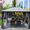 A stylish gazebo with a modern, dark - colored roof stands on a patio adjacent to a home. It is equipped with dark privacy curtains and sheer mesh panels, providing both seclusion and protection from bugs. The gazebo houses a black outdoor dining set, and the area is enhanced by the lush plants and colorful blooms in the background. Modern Outdoor Gazebo: Ideal for Garden Dining. Stylish Gazebo with Mesh and Curtains for Outdoor Relaxation. outdoor gazebo, garden gazebo, mesh netting, privacy curtains