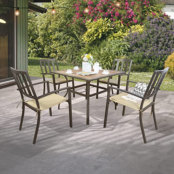A set of outdoor dining chairs with a dark brown metal frame and beige cushions is arranged around a square table on a patio. The scene is set in a garden with greenery and colorful flowers in the background, and string lights are hanging above, creating a cozy outdoor dining atmosphere. Outdoor Dining Chairs: Stylish Seating for Patio Meals. outdoor dining chairs, metal frame chairs, beige cushioned chairs, patio furniture, garden dining