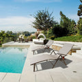 Two beige foldable lounge chairs placed beside a swimming pool in a luxurious outdoor setting. The chairs feature built - in cup holders, perfect for relaxing by the pool. The background includes lush greenery and additional outdoor furniture, enhancing the serene and leisurely atmosphere.Beige Foldable Lounge Chairs by the Pool. beige foldable lounge chairs, poolside lounge chairs, outdoor relaxation, built - in cup holders.