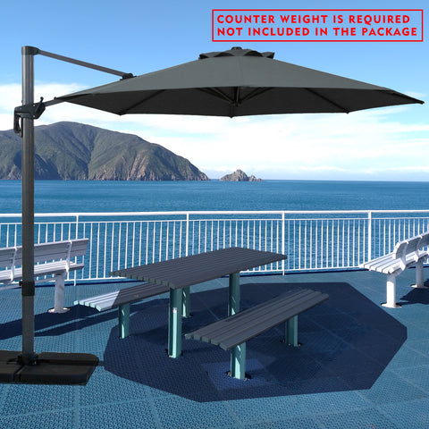 Gray cantilever patio umbrella providing shade over a picnic table by the seaside. Note: Counter weight is required and not included in the package. Outdoor offset umbrella in a coastal setting. It shades an outdoor table, and a counter weight is needed but not part of the package. Seaside Patio Umbrella: Counter Weight Not Included. Cantilever Umbrella for Outdoor Use: Counter Weight Required. cantilever umbrella, patio umbrella, outdoor umbrella, counter weight, umbrella shade