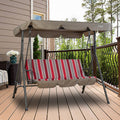 A Kozyard outdoor swing chair placed on a wooden deck of a house. The swing has a sturdy metal frame and is topped with a beige - brown canopy. The seat features a cushion with a striking pattern of vertical red, gray, and white stripes. In the background, there's a house wall, a window, a decorative vase with white flowers, and a railing overlooking greenery, creating a cozy outdoor relaxation spot. Kozyard Outdoor Swing Chair: Comfort and Style on Your Deck. Kozyard swing chair, outdoor patio swing.
