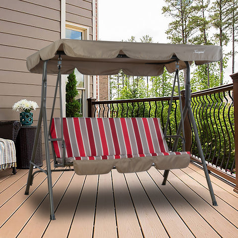 A Kozyard outdoor swing chair placed on a wooden deck of a house. The swing has a sturdy metal frame and is topped with a beige - brown canopy. The seat features a cushion with a striking pattern of vertical red, gray, and white stripes. In the background, there's a house wall, a window, a decorative vase with white flowers, and a railing overlooking greenery, creating a cozy outdoor relaxation spot. Kozyard Outdoor Swing Chair: Comfort and Style on Your Deck. Kozyard swing chair, outdoor patio swing.