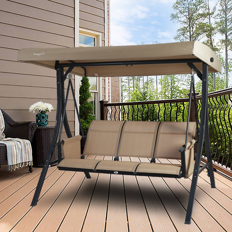 A beige Kozyard swing chair is placed on a wooden deck of a house. The swing features a sturdy black metal frame and a canopy that provides shade. The seating area has a beige fabric, suitable for three people, making it an ideal spot for relaxation on the balcony. Kozyard Beige Swing Chair for Balcony Relaxation. Kozyard swing chair, beige swing, outdoor balcony furniture, three - seater swing, black metal frame.