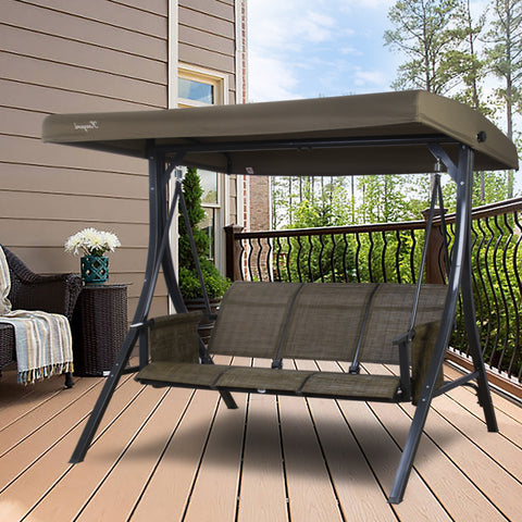 A gray Kozyard swing chair is placed on a wooden deck of a house. The swing features a sturdy black metal frame and a canopy that provides shade. The seating area has gray fabric, suitable for three people, making it an ideal spot for relaxation on the balcony. Kozyard Gray Swing Chair for Balcony Relaxation.Kozyard swing chair, gray swing, outdoor balcony furniture, three-seater swing, black metal frame