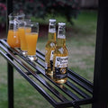 On the black metal shelf of an outdoor barbecue gazebo, there are two bottles of Corona Extra beer and several glasses filled with orange juice. The setting suggests a casual and refreshing outdoor gathering. Refreshments on the Shelf of an Outdoor Barbecue Gazebo. outdoor barbecue gazebo, black metal shelf, Corona Extra beer, orange juice, outdoor gathering