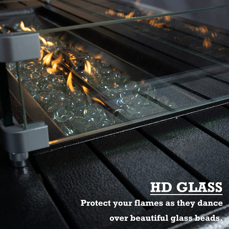 A close - up of the fire pit area of an outdoor fire pit table, showing clear glass beads illuminated by dancing flames. The flames are surrounded by a high - definition (HD) glass barrier. The text "HD GLASS" and "Protect your flames as they dance over beautiful glass beads" emphasizes the protective function of the glass. Outdoor Fire Pit Table with HD Glass Protection. outdoor fire pit table, HD glass barrier, glass beads fire pit, flame protection, patio fire feature