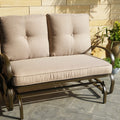A glider chair with beige cushions is positioned on an outdoor stone - tiled area, next to a potted plant and a stone wall. The chair has a sturdy metal frame with curved armrests, providing a comfortable and stylish spot for relaxation.Beige - Cushioned Glider Chair for Outdoor Relaxation.beige - cushioned glider chair, outdoor furniture, metal - framed chair, curved armrests, relaxation