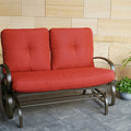 A glider chair with vibrant red cushions is placed on a stone - tiled floor next to decorative plants and a lantern. The chair features a sturdy metal frame with curved armrests, providing a comfortable and stylish spot for relaxation. Red - Cushioned Glider Chair for Relaxing Moments.red - cushioned glider chair, metal - framed glider, outdoor relaxation, curved armrests.